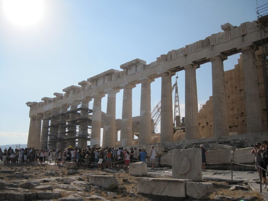 Crowds of people around the Parthenon in Athens, Greece with scaffolding and a construction crane visible.