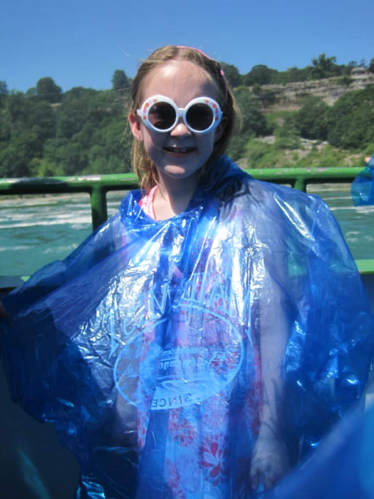 Young girl with white sunglasses in blue poncho on deck of the Maid of the Mist in Niagara Falls, Canada.