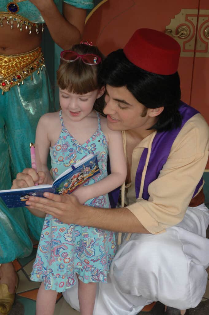 Young girl talking to Aladdin as he signs her autograph book at Disney World in Orlando, Florida.