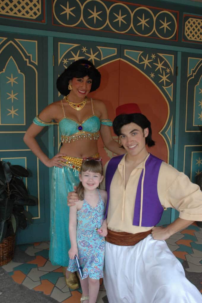 Princess Jasmine standing and Aladdin kneeling with arm around young girl at Disney World.