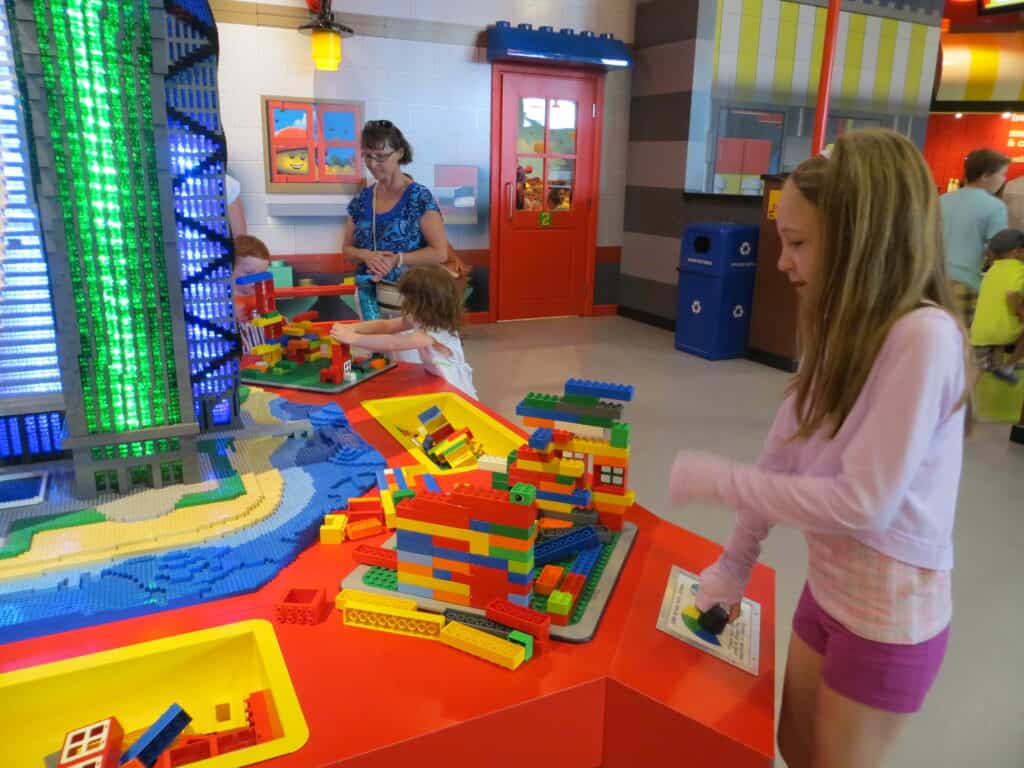 Young girl in light pink long-sleeved top and dark pink shorts plays at multi-coloured Earthquake table at LEGOLAND Discovery Centre Toronto.