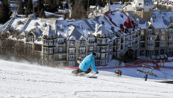 Skier in bright blue jacket coming down ski slope with Mont Tremblant Village in background.