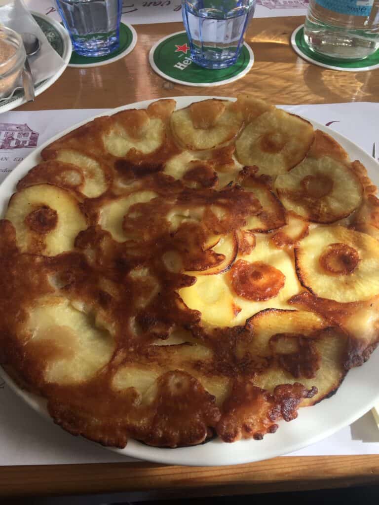 Large apple pancake on white plate sitting on a restaurant table with glassware in background - Edam, Netherlands.