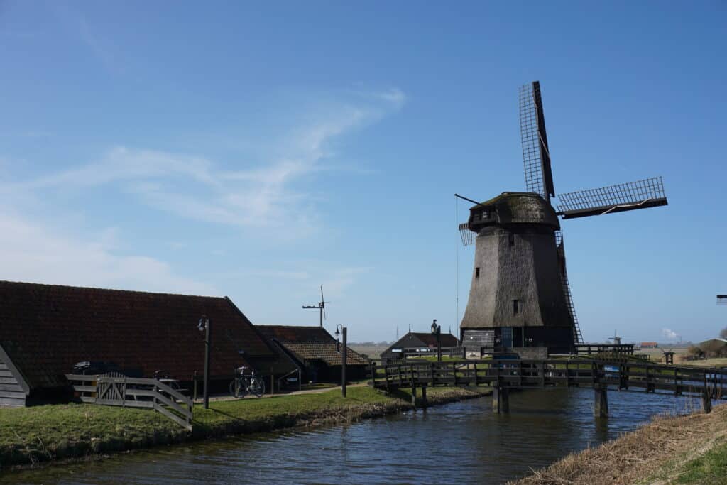 Windmill and other buildings and fence alongside a small canal in the Dutch countryside.