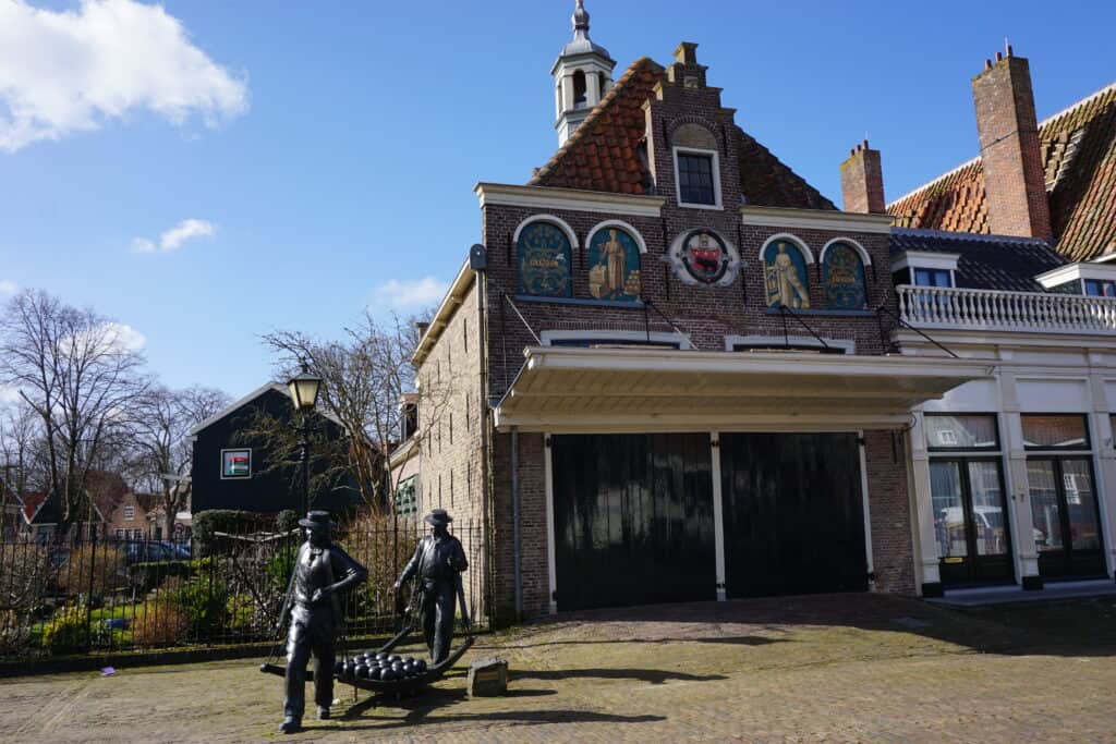 Bronze sculpture of two men hauling rounds of cheese in front of the Cheese Market building in Edam, Netherlands.