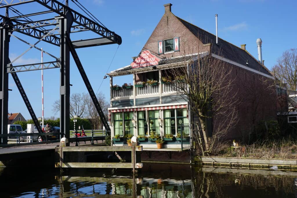 Hof Van Holland Restaurant in Edam - three story wooden building with windows on first level, balcony with flowers on second and a single window on third - beside canal.