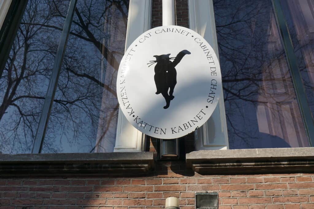 White circular sign with black cat and words outside Kattinkabinet museum in Amsterdam.