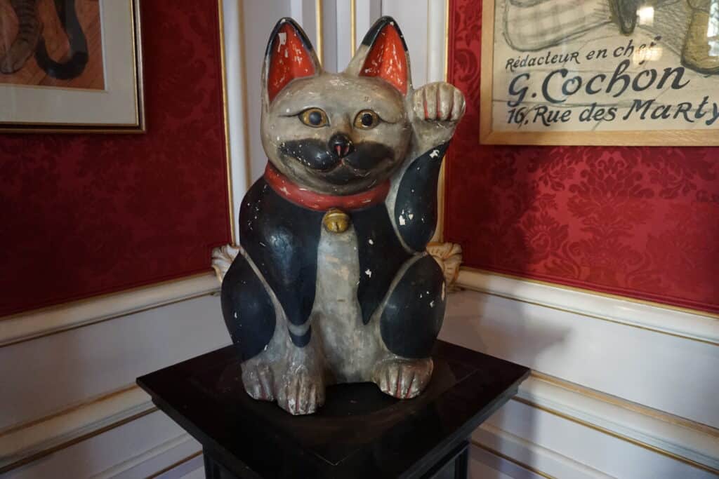 Large black, white and red cat porcelain figurine on display in a corner of Kattinkabinet with red wallpaper, white trim and framed artwork on wall behind - Amsterdam.