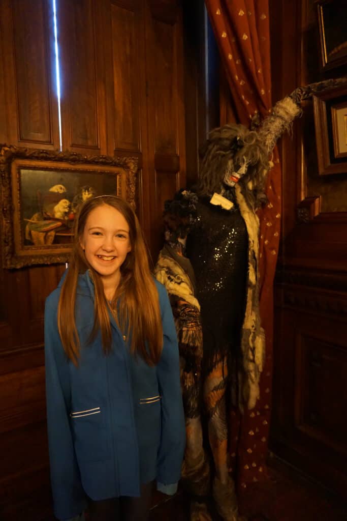 Young girl in blue jacket posing in front of display of Grizabella costume from Cats the Musical at Kattinkabinet in Amsterdam.