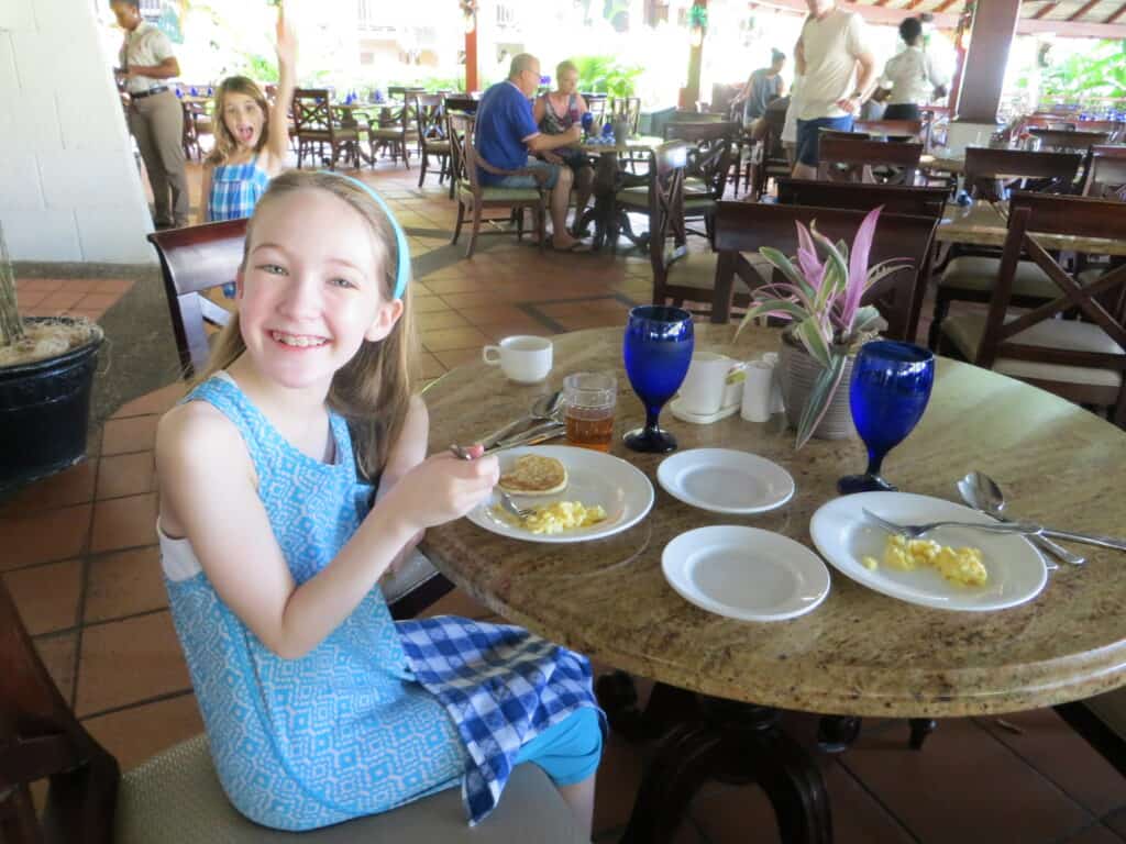 Young girl in blue dress eating breakfast at a table in restaurant at Beaches Resort Negril.