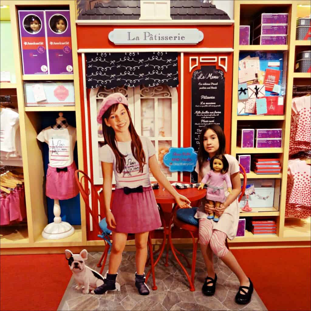 Young girl holding doll sitting on red chair at American Girl doll of the year display.