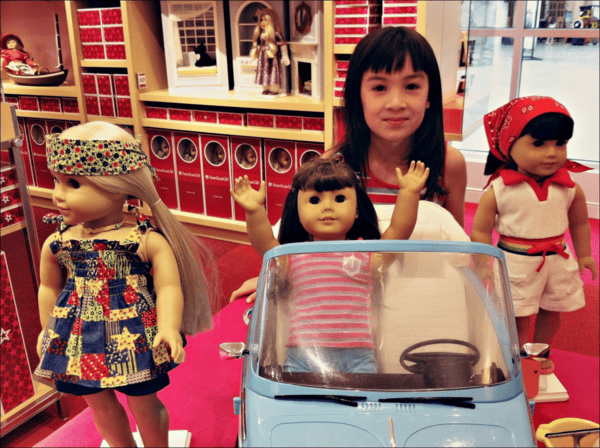 Young girl with Julie American Girl Doll display - doll in light blue VW convertible and two other dolls on display.