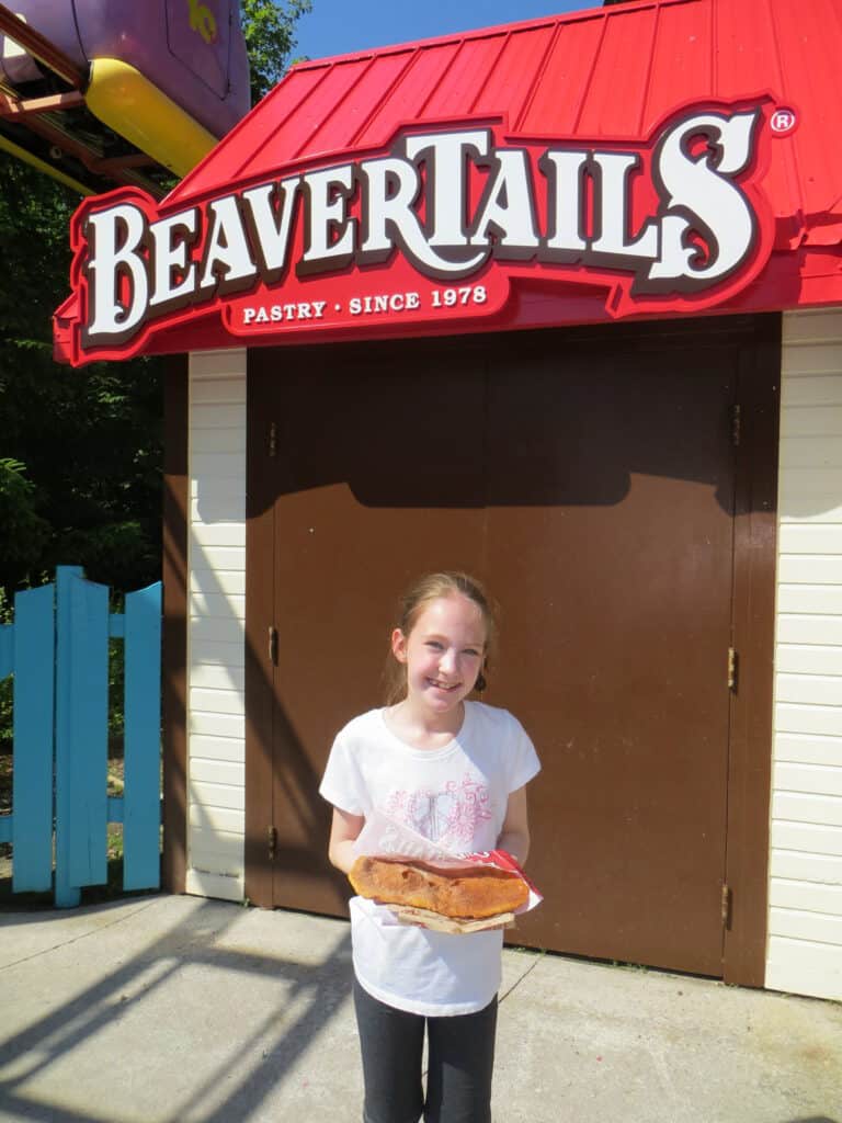 Young girl holding BeaverTails pastry in front of BeaverTails sign at Canada's Wonderland.