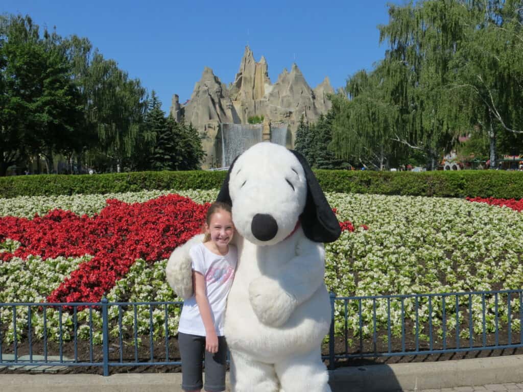 Young girl posing with Snoopy in front of Canada flag garden at Canada's Wonderland.