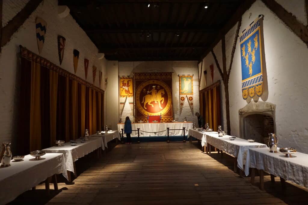 Recreated banquet hall in Dover Castle - tables with white cloths and silver tableware at head of room and along perimeter and banners hanging on walls.