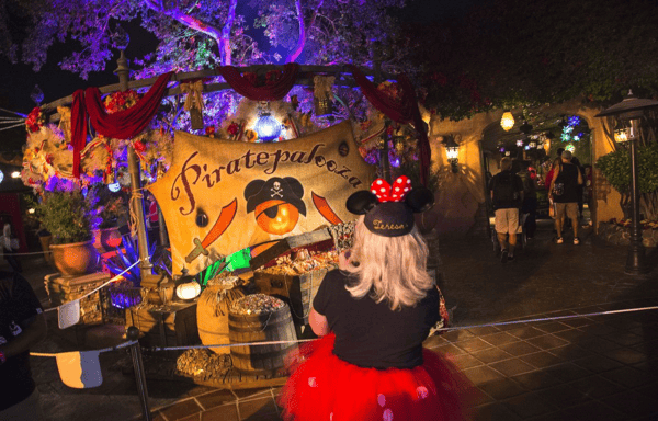 Young girl in costume at Disneyland trick or treating in front of a sign saying Piratepalooza.