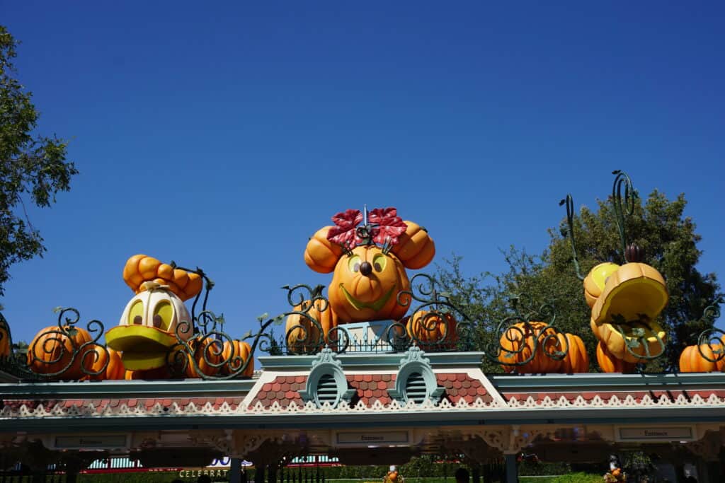 Entrance to Disneyland at Halloween with Donald Duck, Minnie Mouse and Pluto jack-o-lanterns set against bright blue sky.