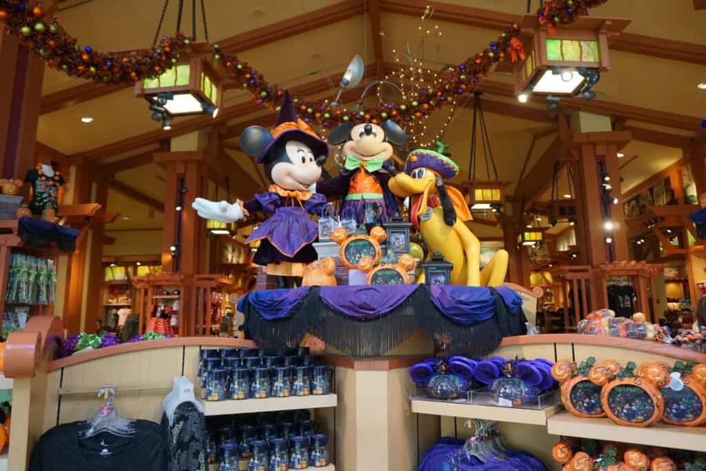 Large figurines of Mickey, Minnie and Pluto in Halloween costumes above a display of Halloween merchandise in a Disneyland shop.