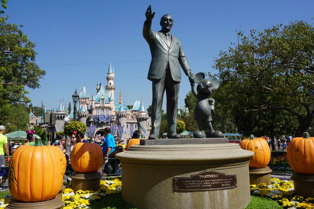 Statue of Walt Disney and Mickey Mouse surrounded by jack-o-lanterns with Sleeping Beauty's castle in the background at Disneyland.