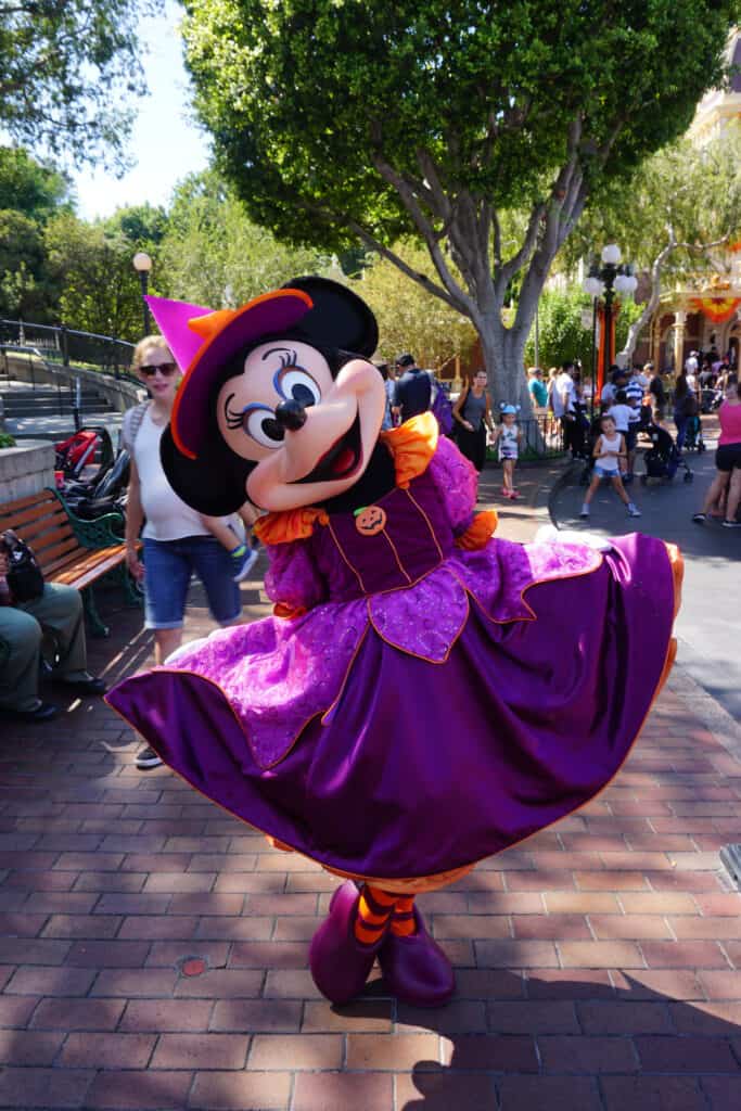 Minnie Mouse posing in purple and orange halloween dress and hat.