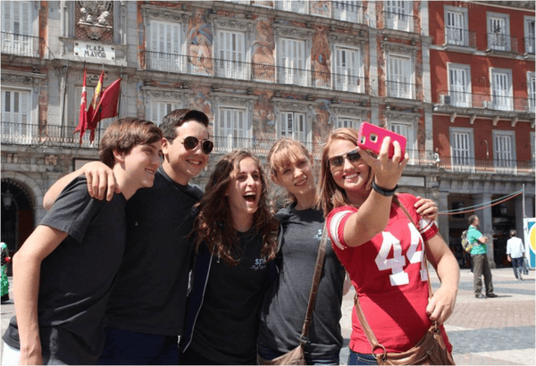 Group of 5 teens taking selfie in front of building.