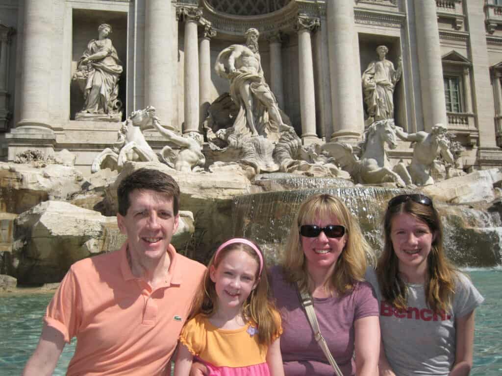 Man, woman, teen girl and younger girl sitting in front of the Trevi Fountain in Rome, Italy.