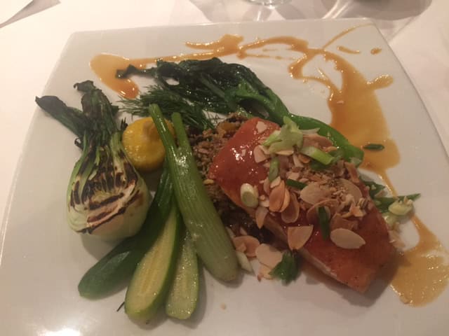 plate of salmon and vegetables topped with slivered almonds and sauce on white plate.