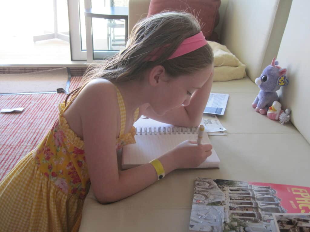 Young girl kneeling on floor and writing in journal sitting on the sofa in cruise stateroom.