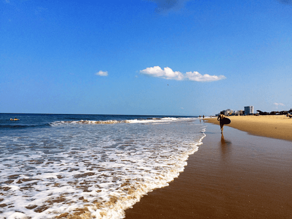 Man with surfboard walking on Virginia Beach.