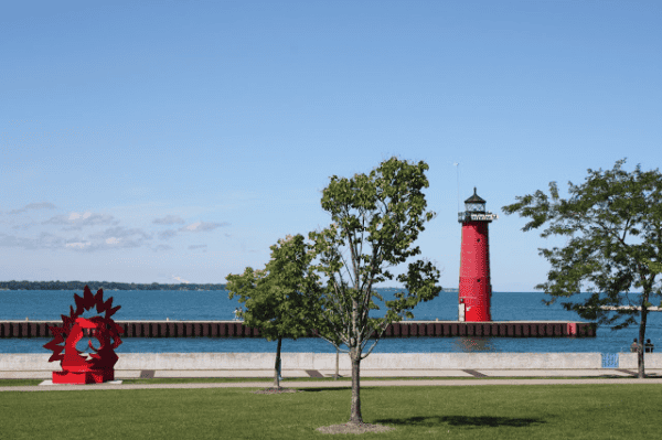 Red lighthouse on waterfront in Kenosha, Wisconsin with two trees in foreground.