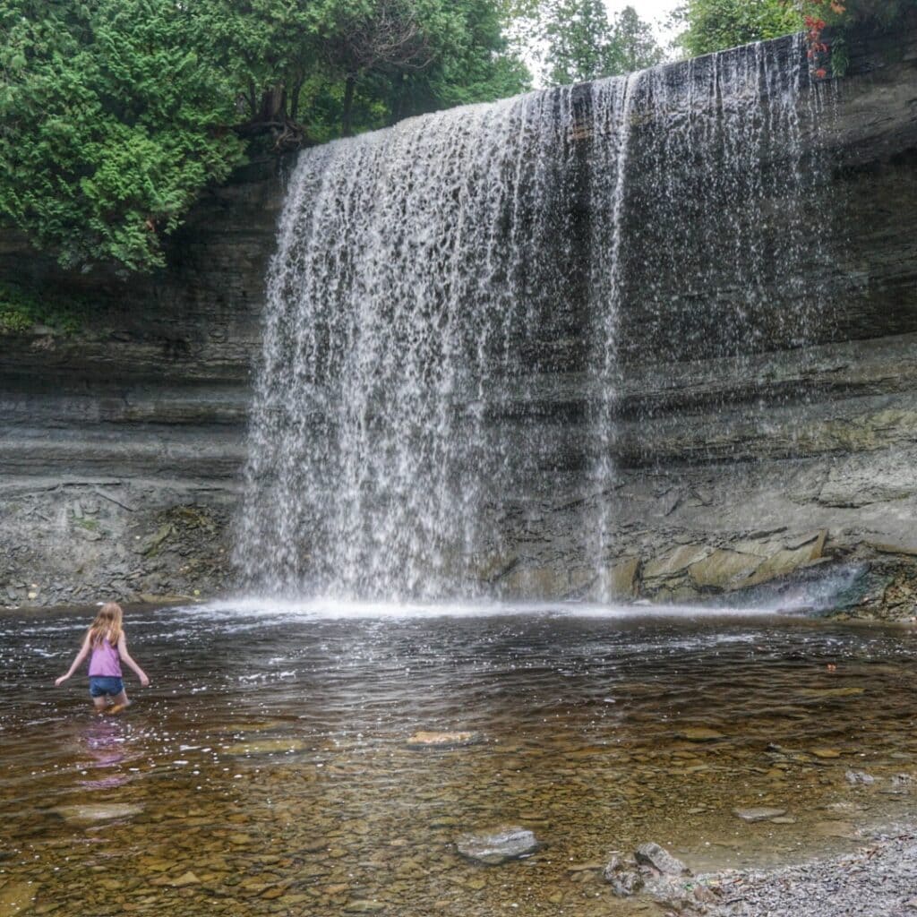 Young girl in shorts and tank top in water in front of Bridal Veil Falls, Manitoulin Island.