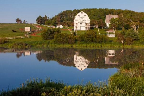 White building with words Anne of Green Gables Museum on farm property and reflected in water, Silver Bush, Prince Edward Island.