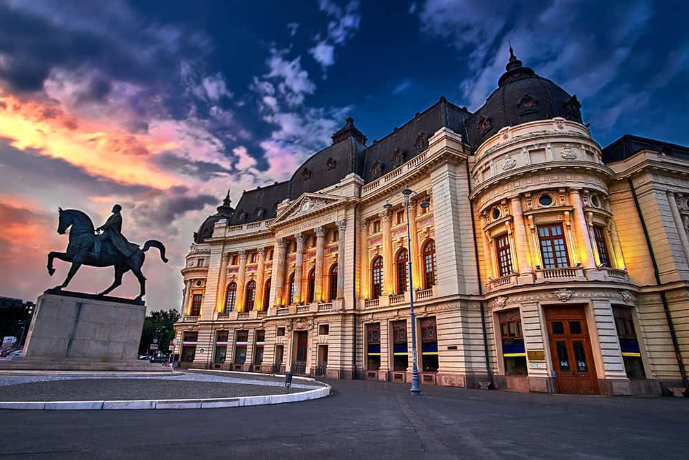 Grand building with statue of man on horse in Bucharest, Romania as sun is setting.