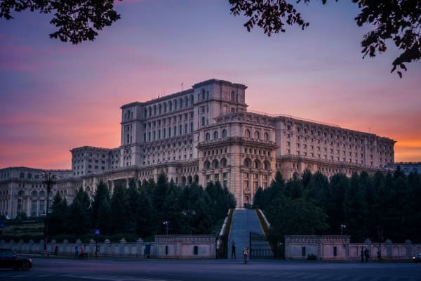 Palace of Parliament in Bucharest, Romania at sunset with pinkish/orange sky.