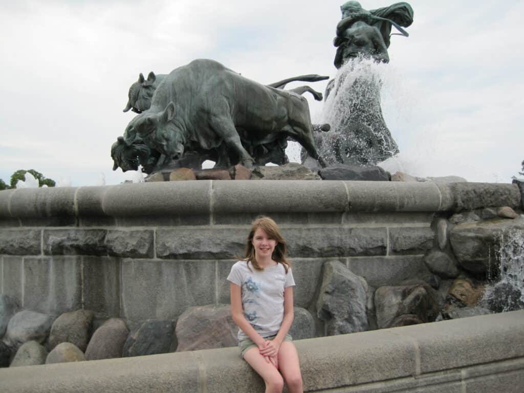 Young teen girl in shorts and t-shirt sitting in front of Gefion Fountain in Copenhagen.
