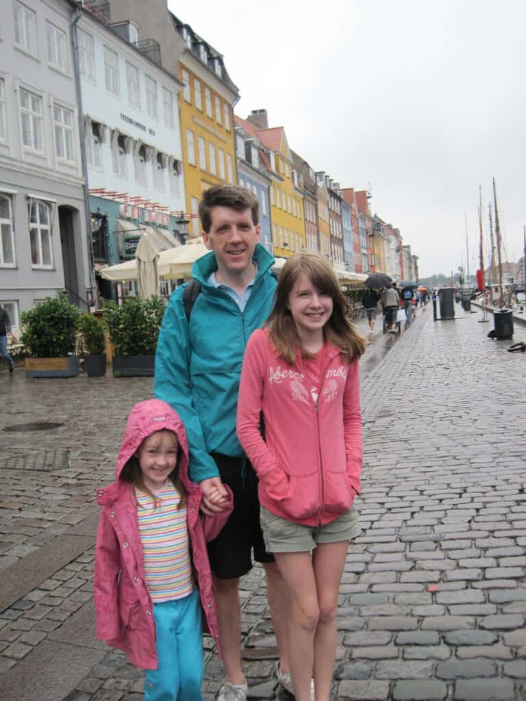 Man, teen girl and young girl posing in front of colourful Nyhavn buildings in rain, Copenhagen, Denmark.