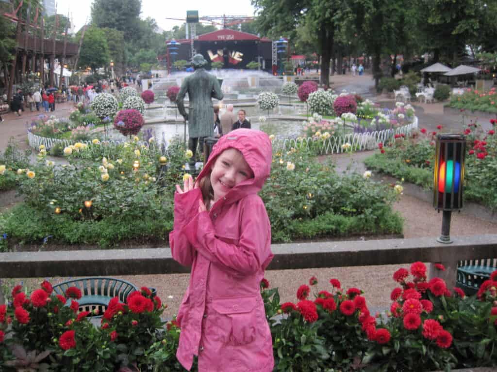 Young girl in pink raincoat with hood up standing in flower gardens on a rainy day at Tivoli Gardens in Copenhagen.
