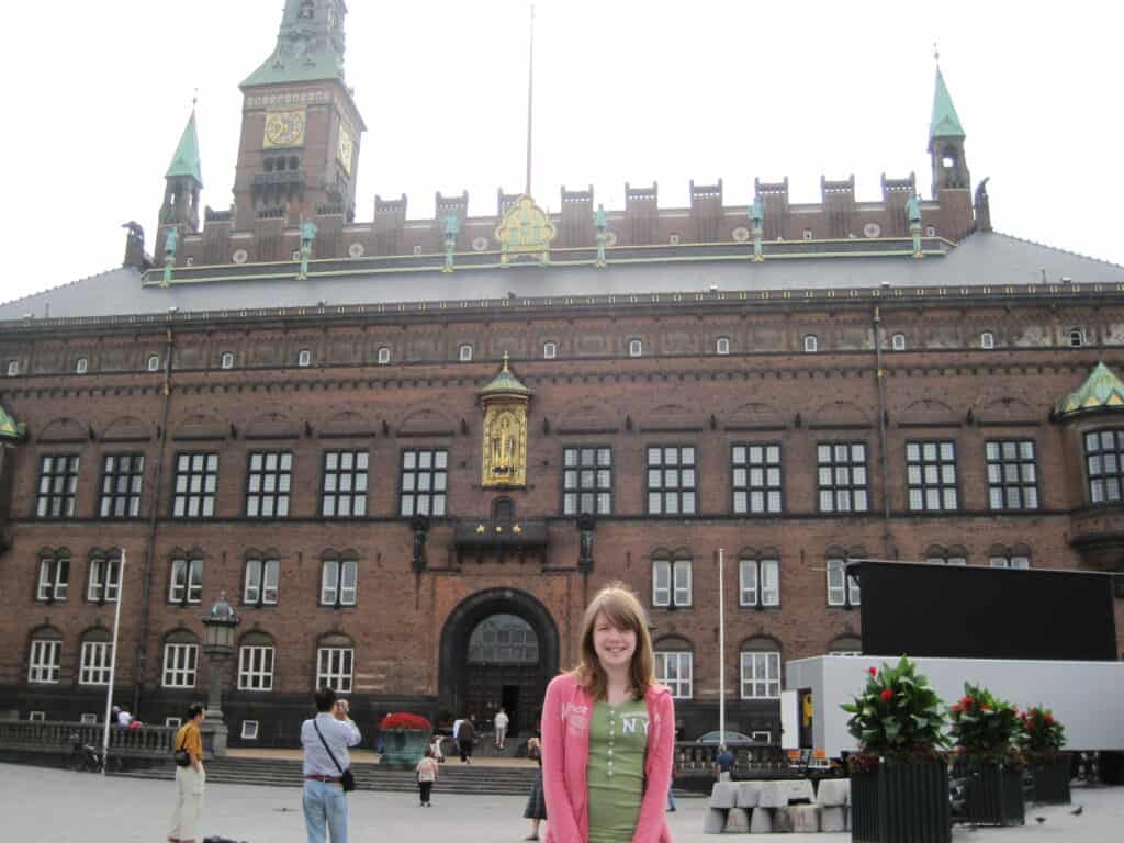 Teen girl in green t-shirt and pink sweatshirt standing outside Radhuset in Copenhagen.