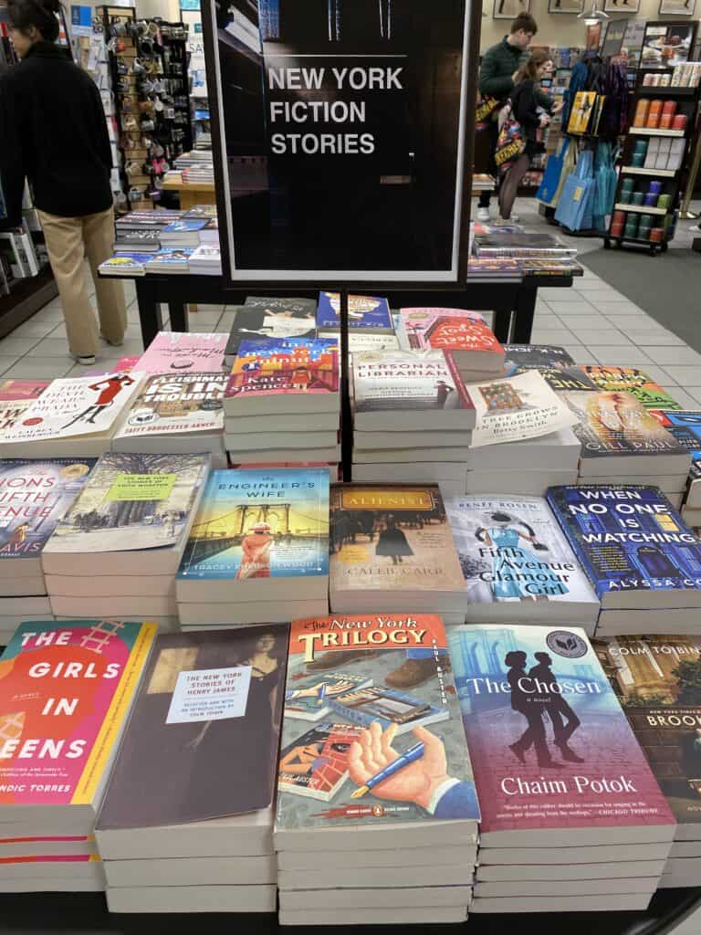 Table in McNally Jackson book store with sign reading "New York Fiction Stories" and stacked with novels set in New York City.