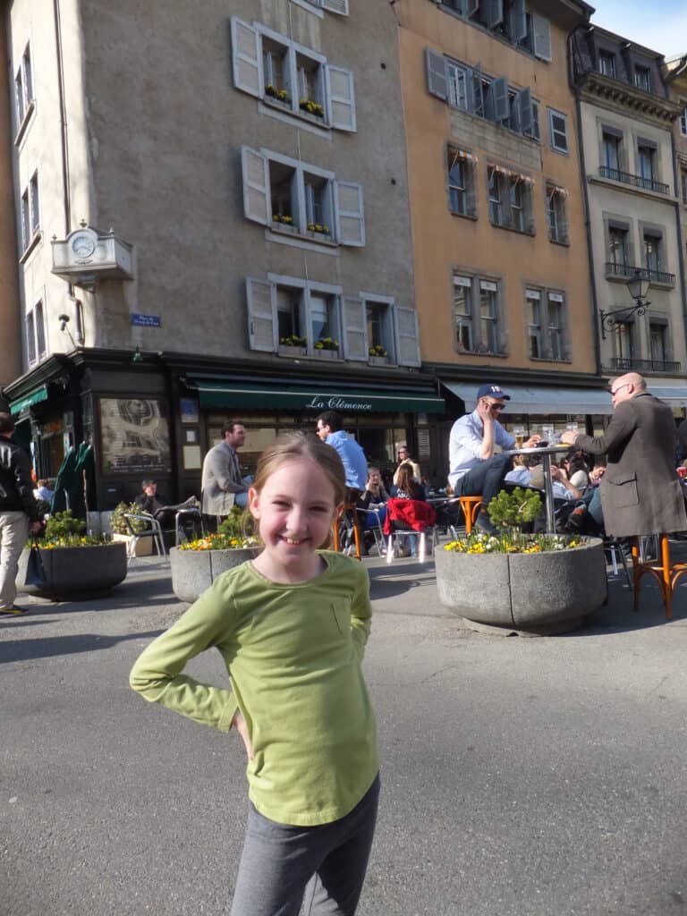 Young girl in green long sleeved t-shirt posing in front of outside dining area of La Clemence in Geneva's Old Town. 