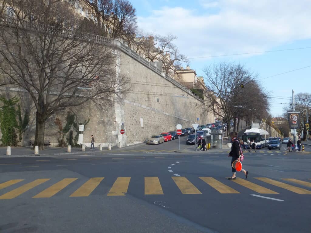 Person crossing street and cars parked along the rampart wall around Geneva's Old Town.