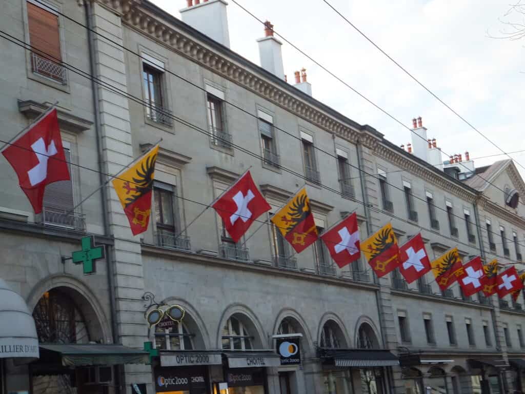Alternating flags of Switzerland and the Canton of Geneva flying on building on a street in Geneva.