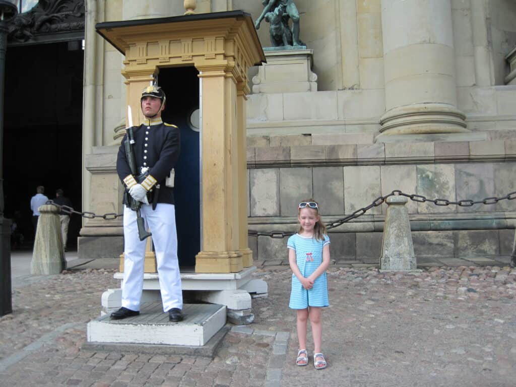 Young girl in blue dress standing beside guard at the Royal Palace in Stockholm, Sweden.