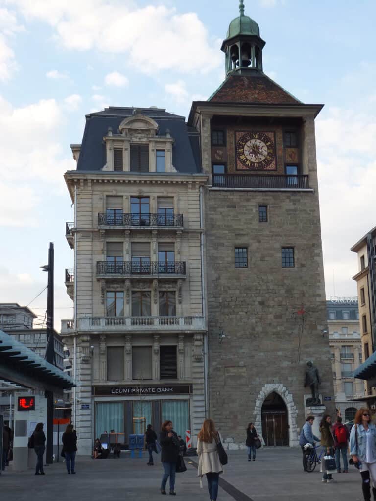 People standing around front of the Tour de L’Île clock tower building in Geneva.