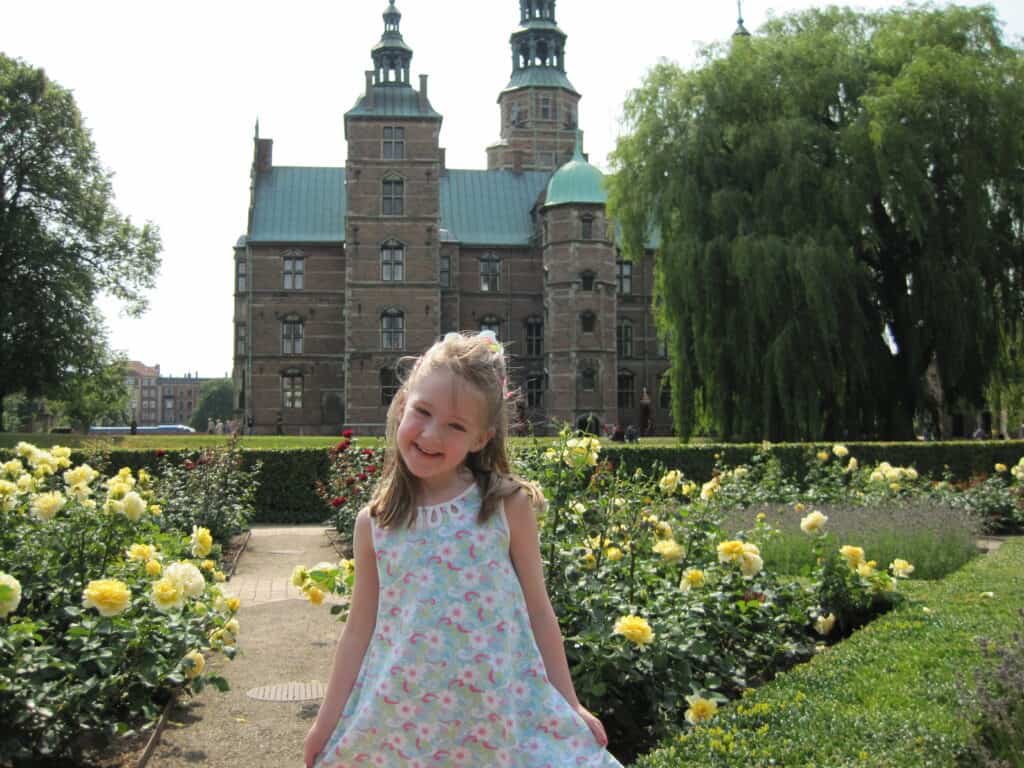 Young girl in blue flowered dress in gardens at Rosenborg Slot in Copenhagen.