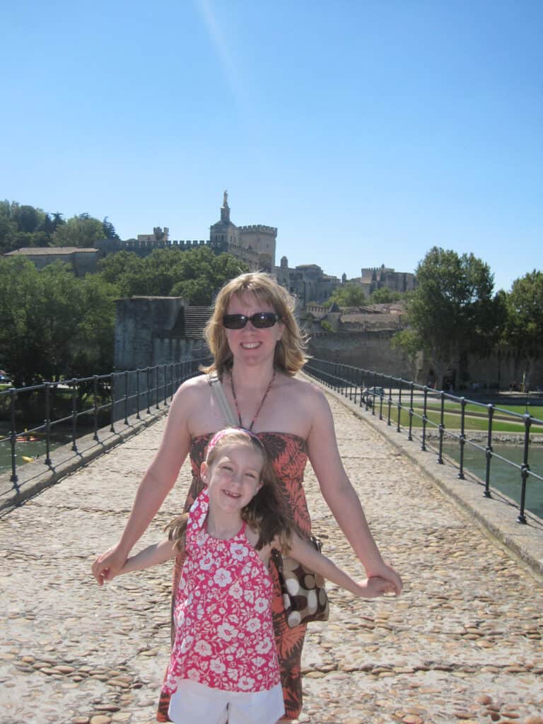 Mom standing behind daughter holding her hands as they dance on the pont d'Avignon.