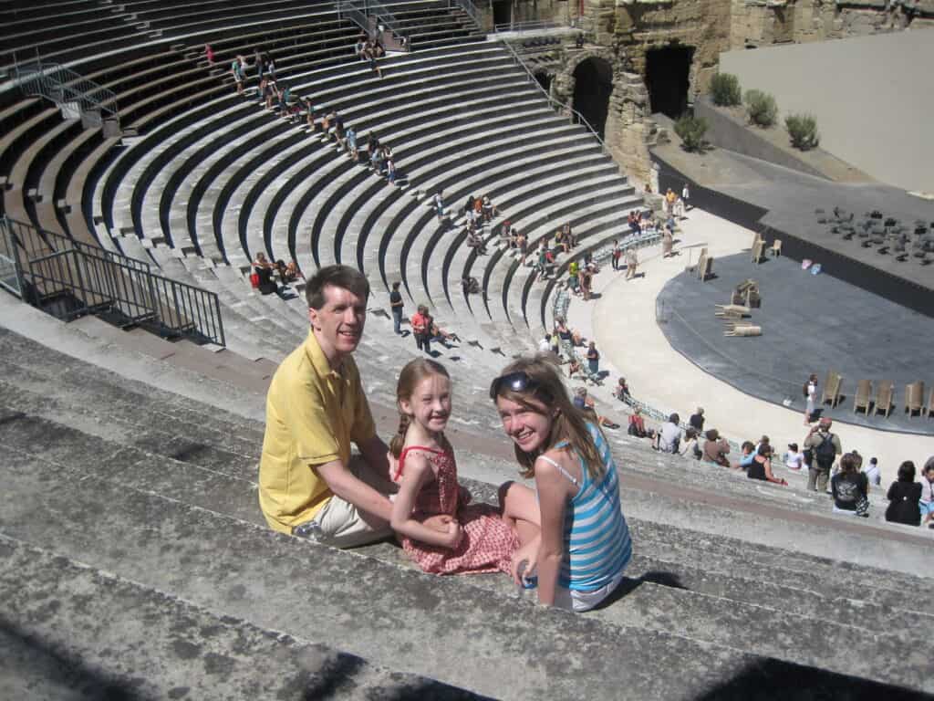 Dad, teen and younger girl sitting in the stands at the Roman Theatre in Orange, France.