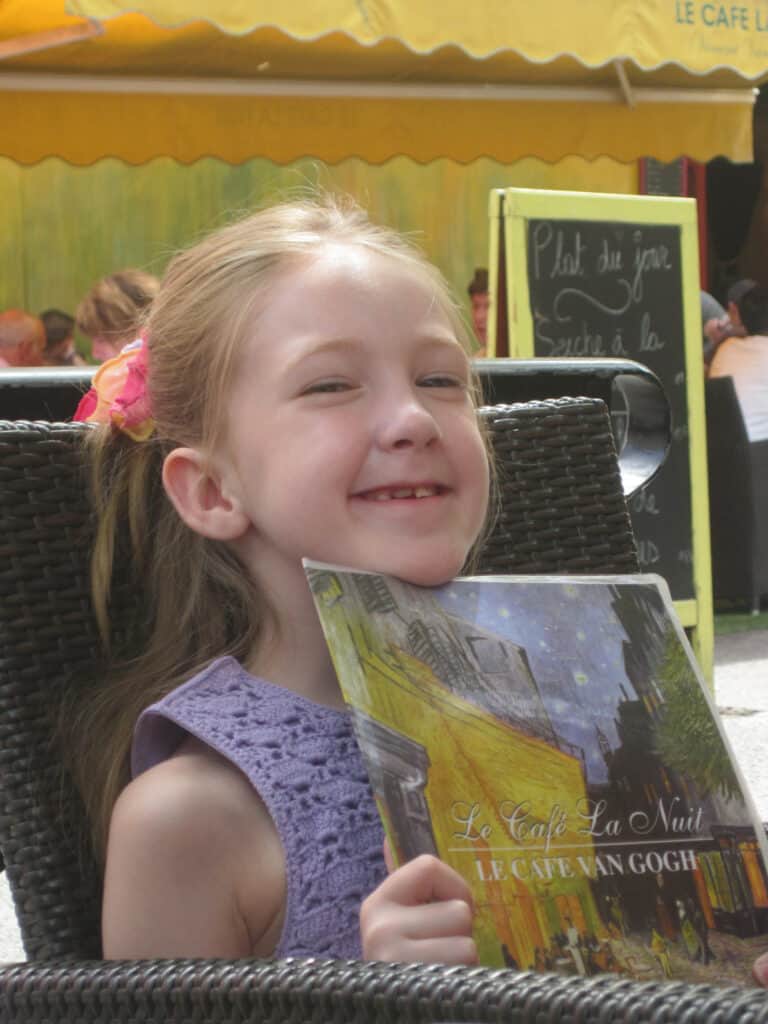 Young girl in purple tank top holding menu for Le Cafe Van Gogh in Arles, France.