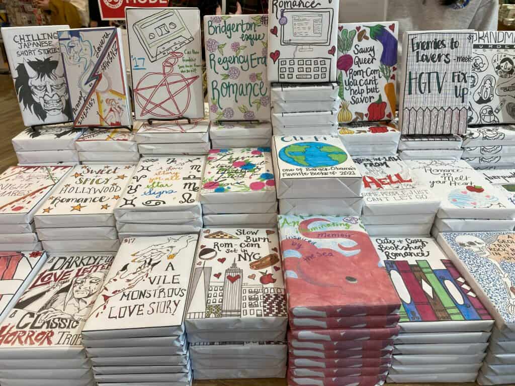 Table display of books wrapped in white paper with sketched illustrations and description of book written on cover at Strand Bookstore in New York City.