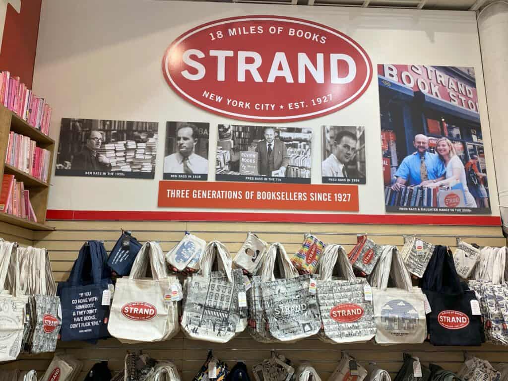 Display of tote bags at the Strand Bookstore beneath Strand sign and photos of three generations of owners.